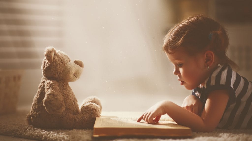 little girl reading to her teddy bear