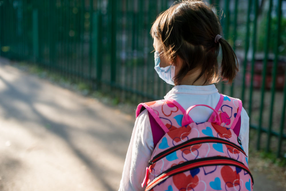 school aged girl with dark brown hair, medical mask, and backpack