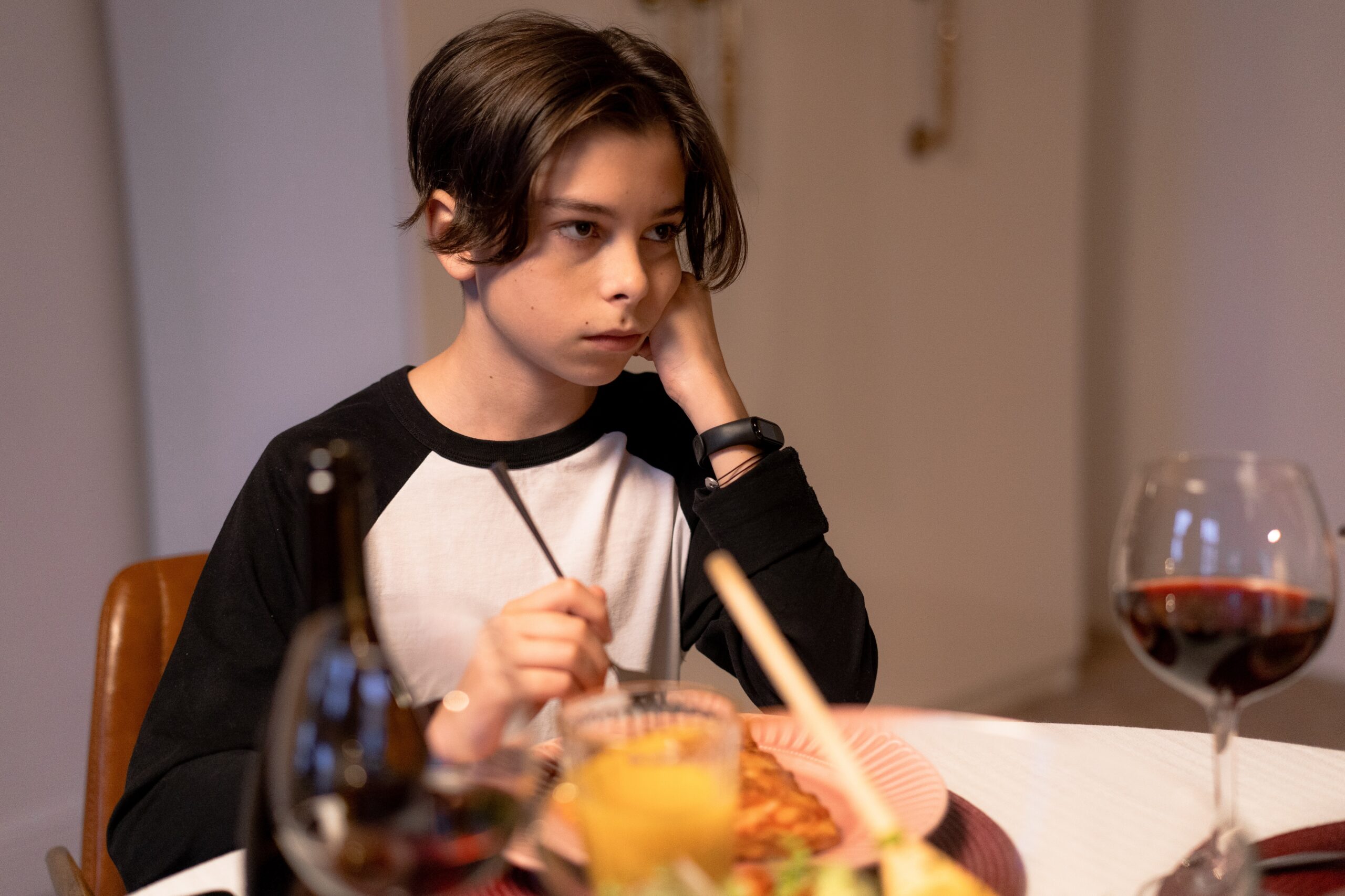 A young boy sits unhappily at the dinner table, feeling disconnected from his parents.