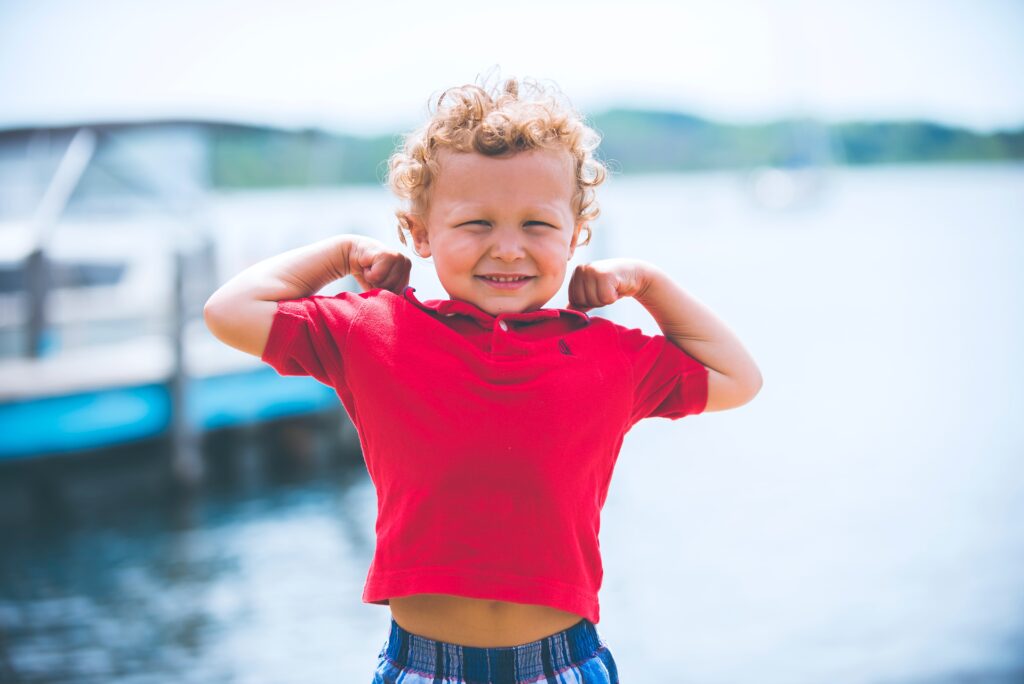 Happy child showing how strong and confident he is, standing on a dock by the water.