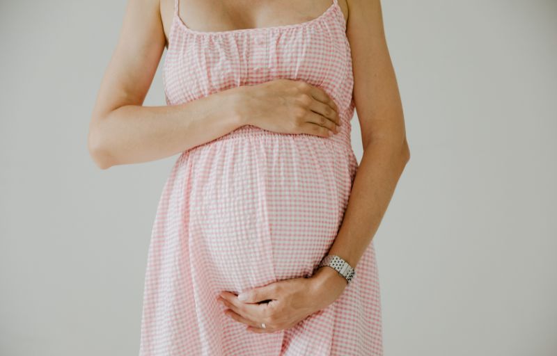Woman holds her pregnant belly, wearing a pink dress.