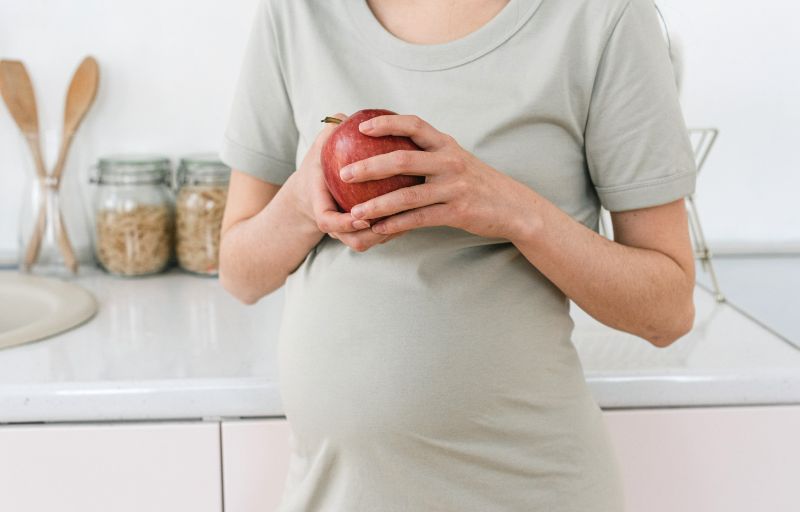 A pregnant woman is holding an apple to eat as a healthy snack to manage her pregnancy nausea.