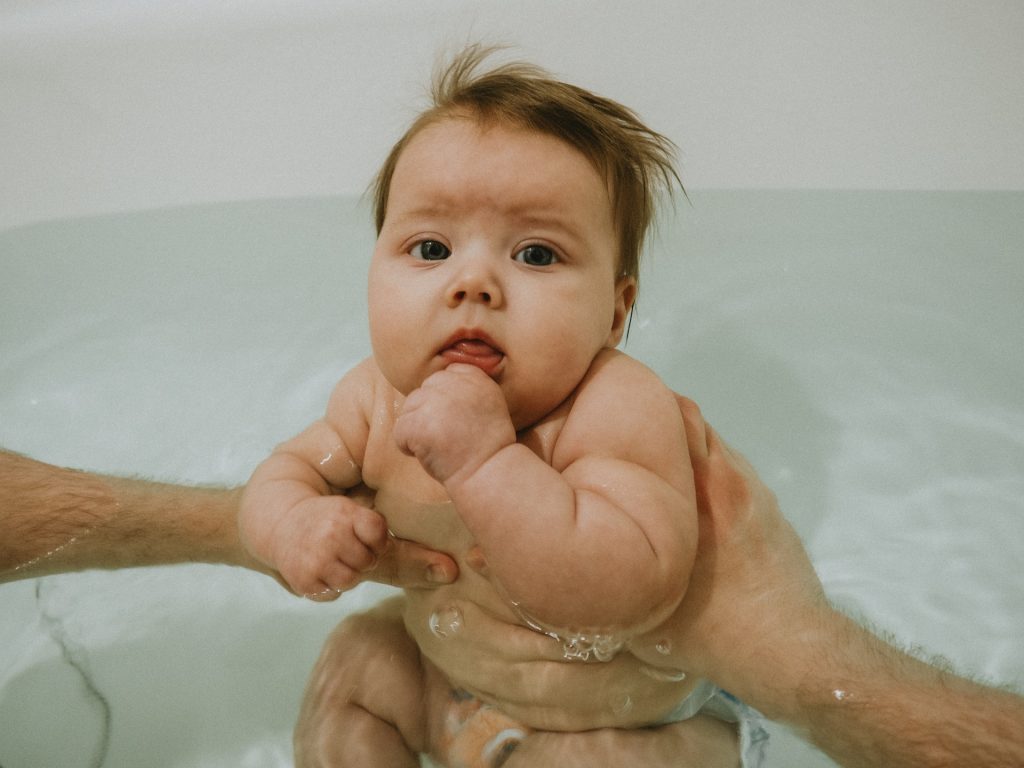 Dad's arms are seen holding the baby in a tub of water to help during witching hour 