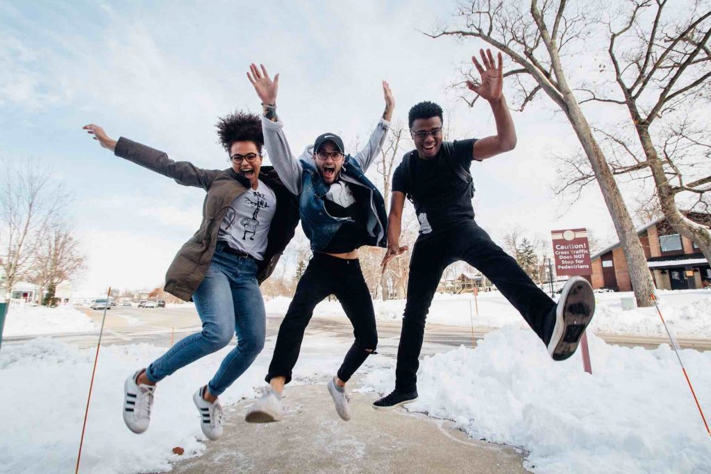 Three people do a jump pose for the camera with snow on the ground behind them