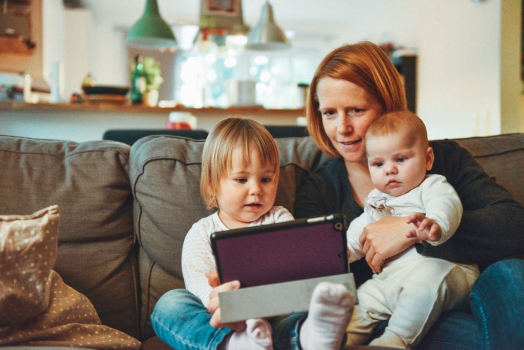 a mother with two children on her lap, looking at a tablet. 