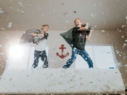 Two boys jumping on the bed, having a pillow fight