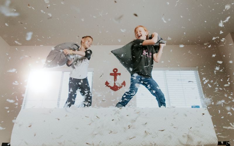 Two boys jumping on the bed, having a pillow fight