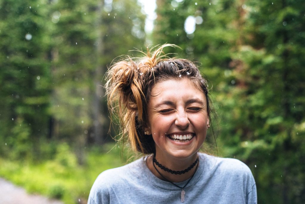 A teen girl walking down a forest path closes her eyes as she laughs