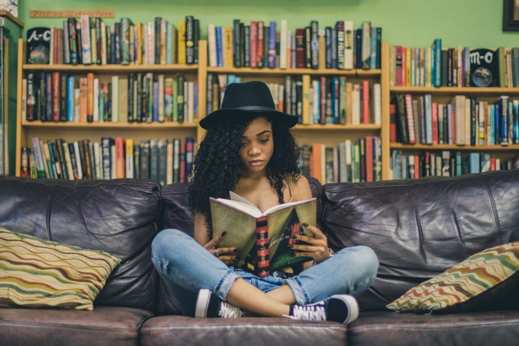 A teen girl sits on a couch while reading a book