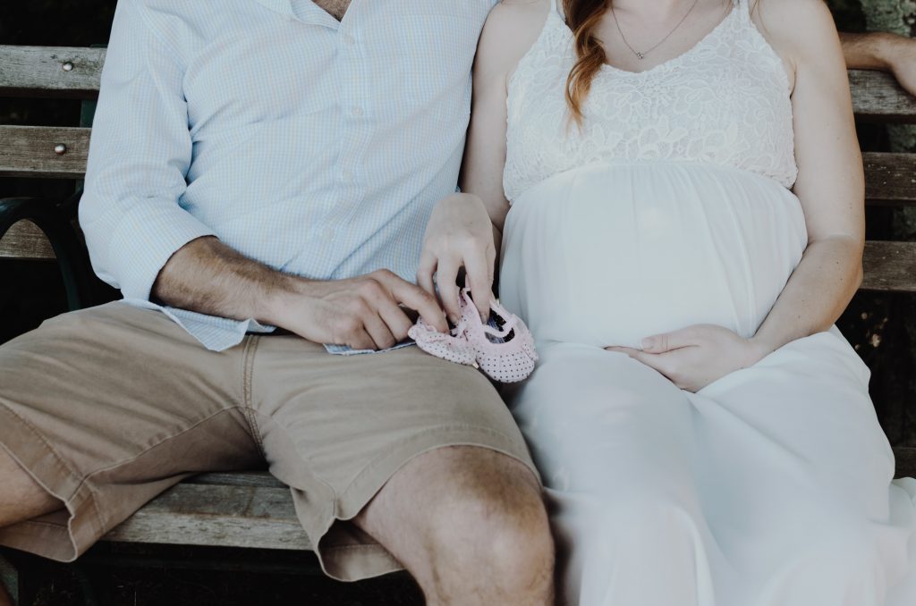 Pregnant woman sitting with her partner on a bench holding baby shoes. 