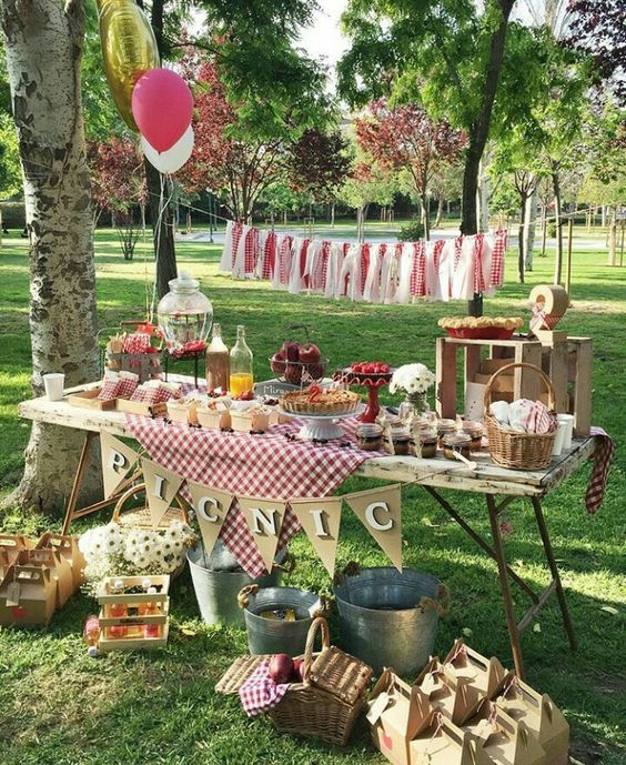 Picnic birthday party table full of birthday party foods and decors in a green park.
