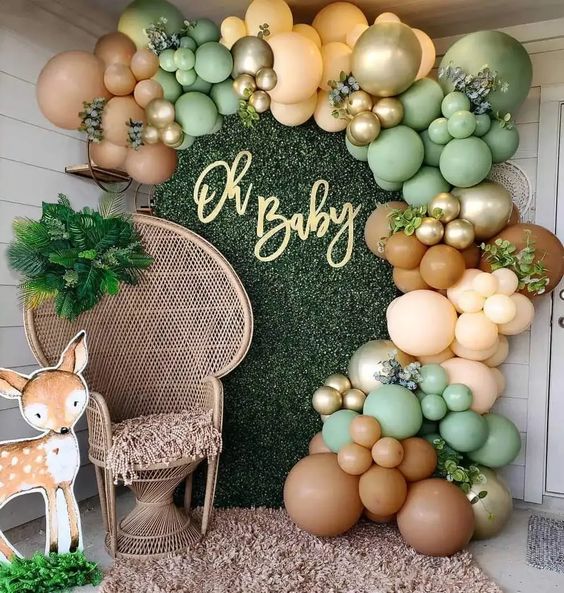 Safari birthday party backdrop with a rattan chair and lots of green and bown balloons.