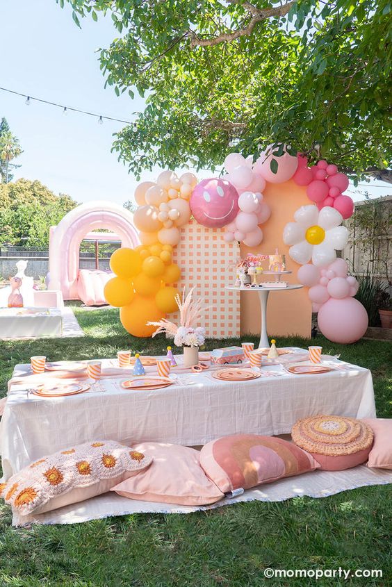 Picnic birthday party set-up showing a colorful backdrop, blakets on the ground, and table with utensils, plates, and snacks.