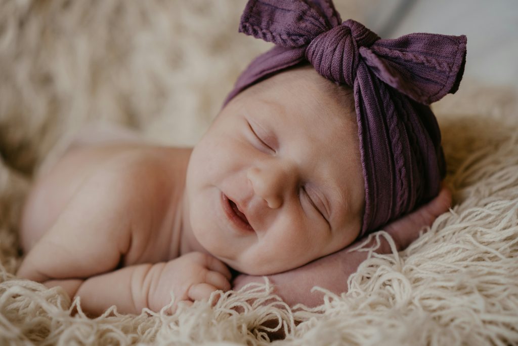Sleeping baby wearing a purple ribbon headpiece.