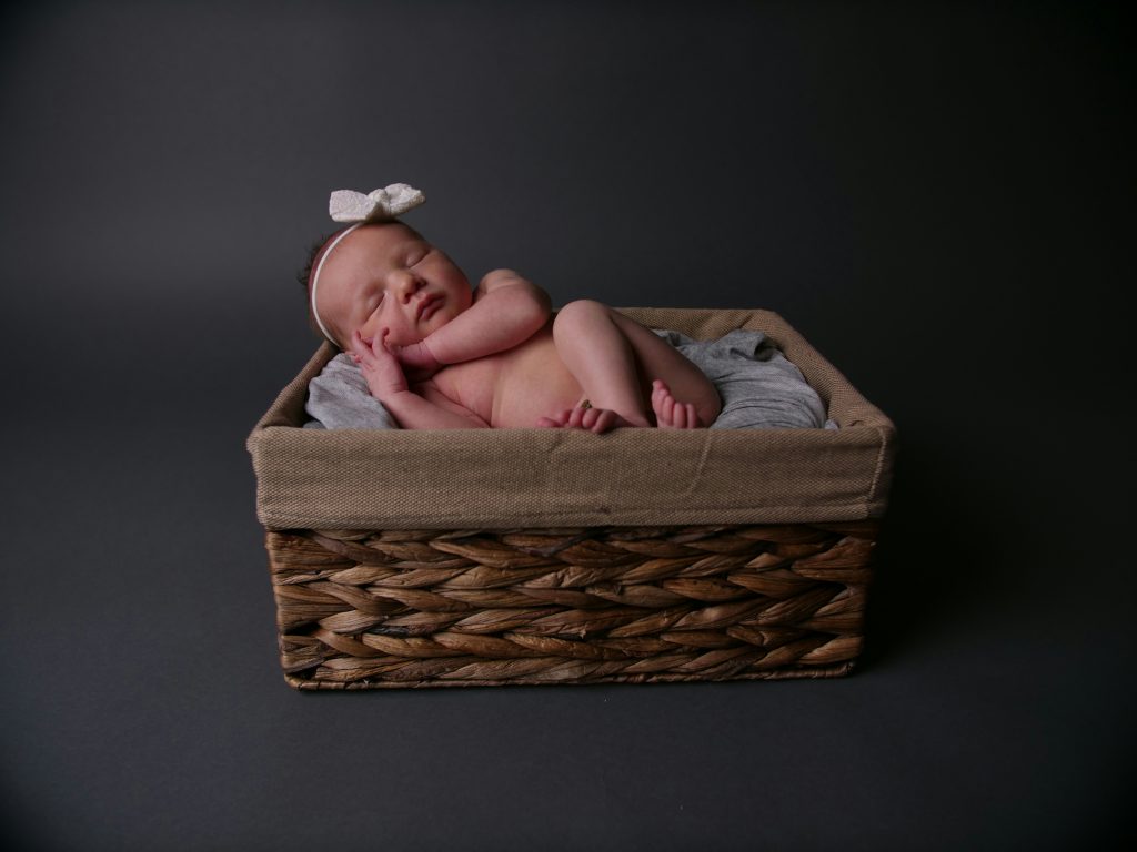 Sleeping newborn baby girl with a ribbon headpiece in a basket.