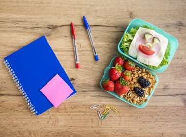 Appetizing school lunch and stationery on a table.