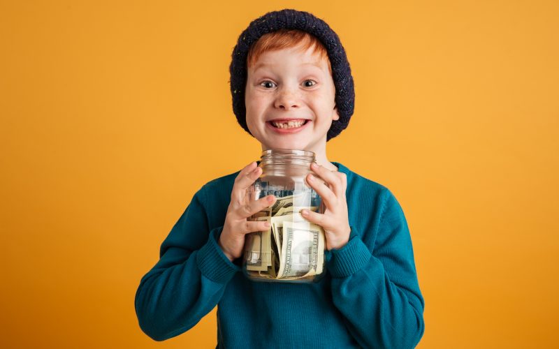 Photo of a little boy with freckles holding a jar of money.