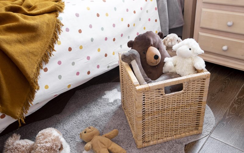 A rattan basket with stuffed animals on a bedroom floor.