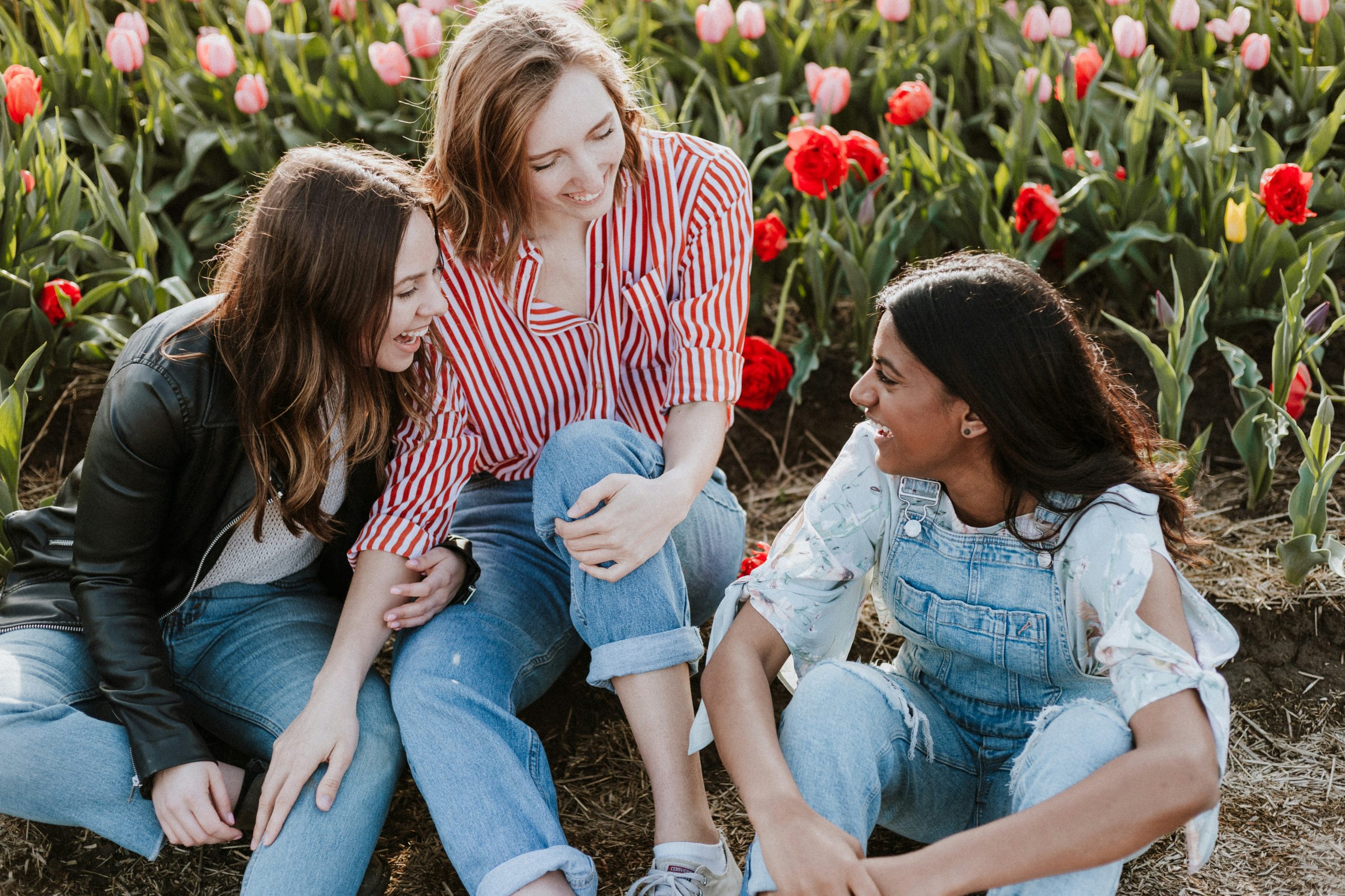 three teen girls laughing in a field of flowers. 