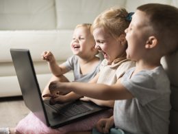 Toddler siblings laughing and pointing at a laptop screen.