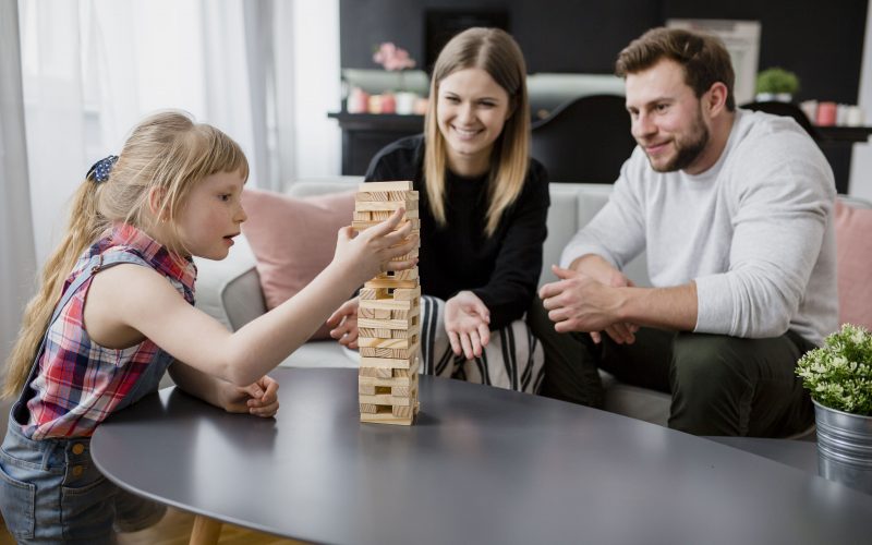 Mom and dad looking at their daughter as she plays jenga.