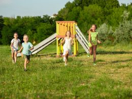 Four kids running down the meadow during summer.