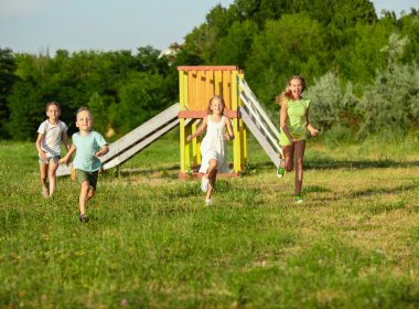 Four kids running down the meadow during summer.